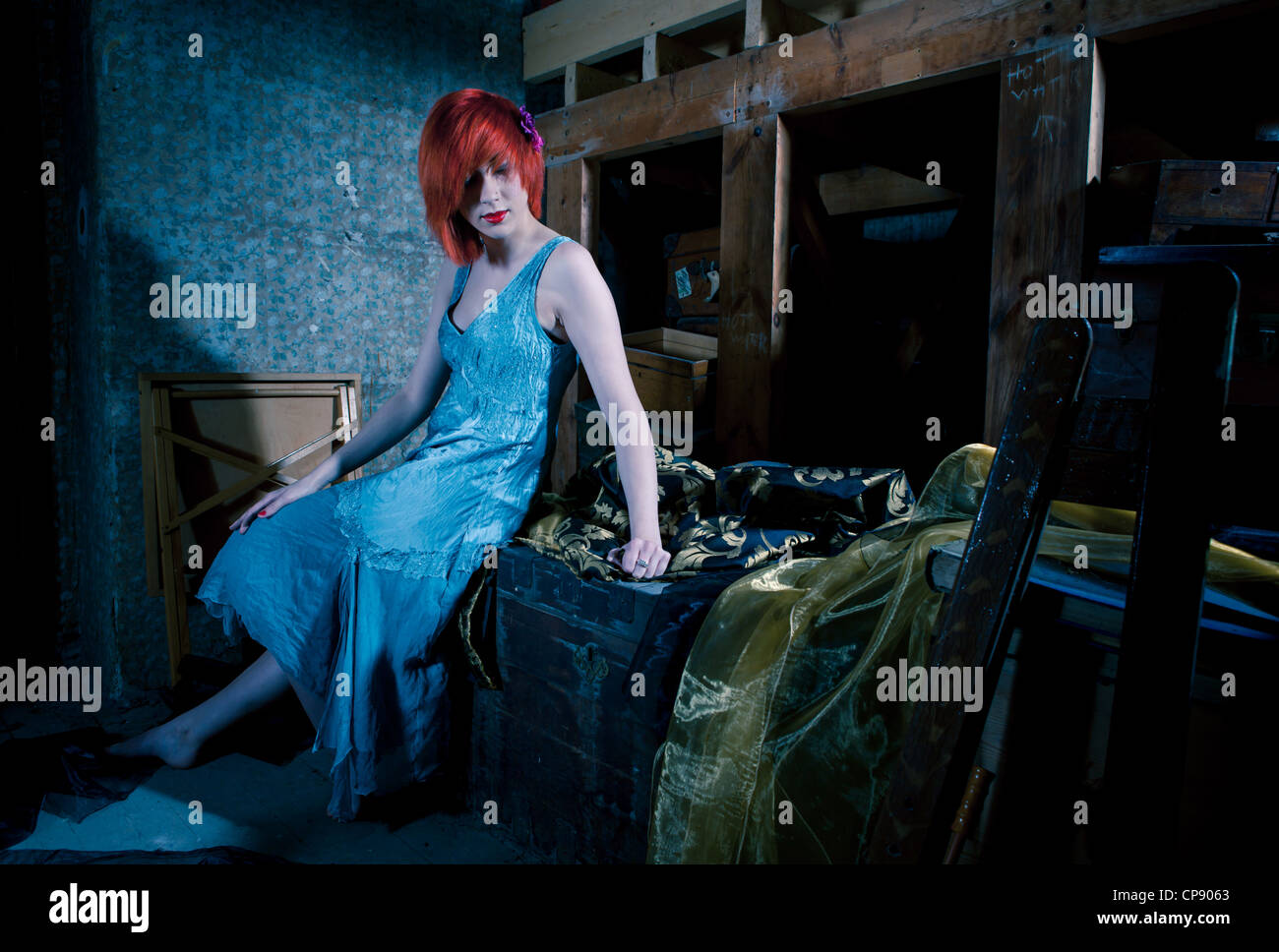 Un attraente giovane donna che indossa un blu abito in seta seduto da solo in un attico Foto Stock