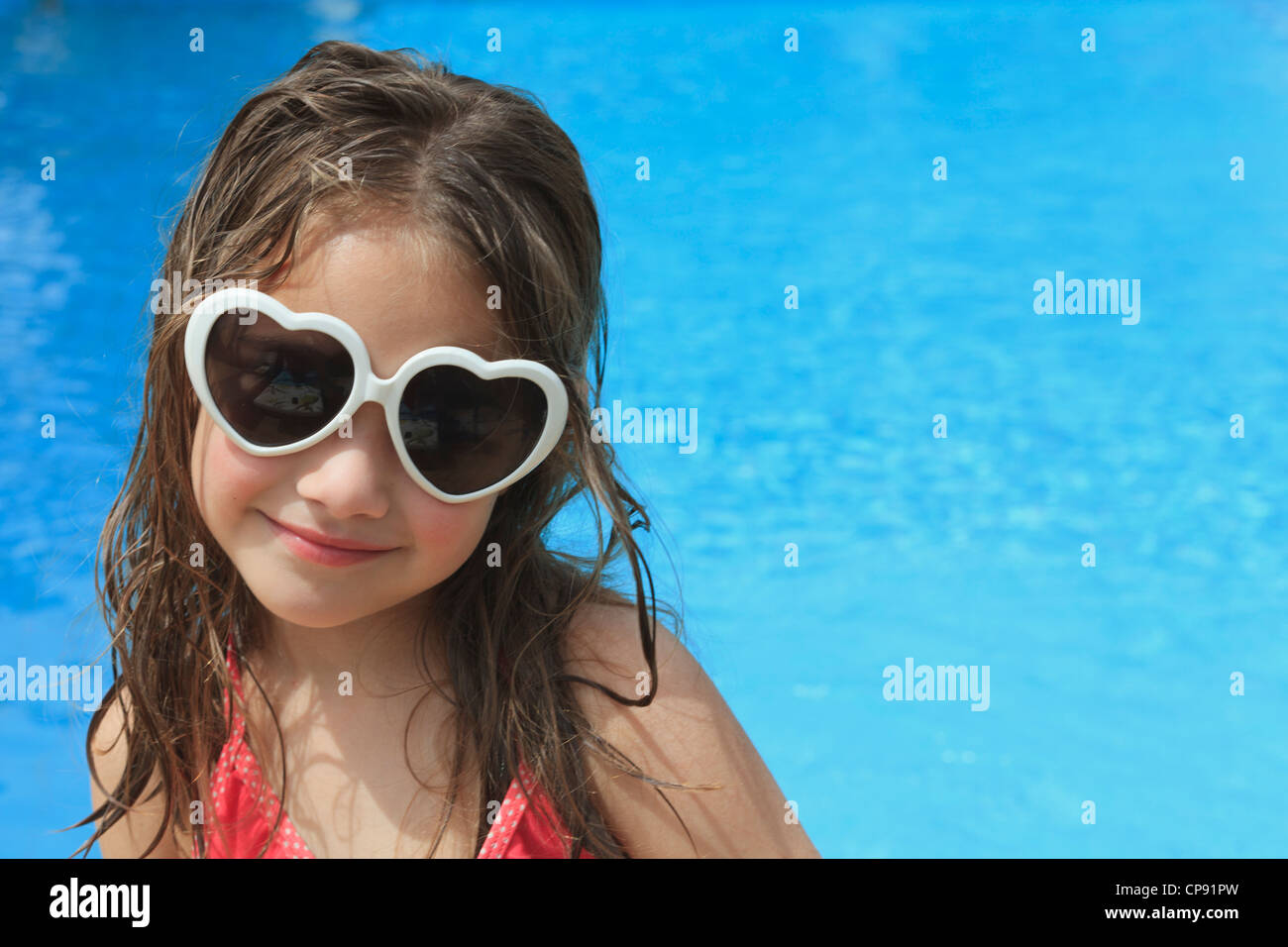 Ragazza giovane da una piscina indossando occhiali da sole Foto Stock
