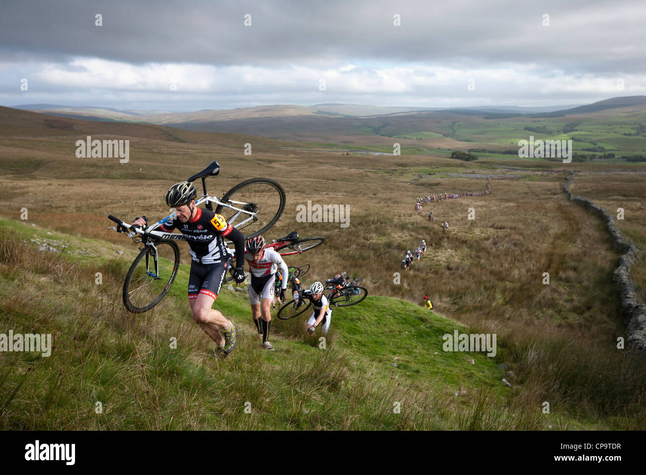 I ciclisti portano le loro biciclette su per una collina ripida durante le Tre Cime di Lavaredo Cyclo-Cross nel North Yorkshire, Inghilterra, Regno Unito Foto Stock