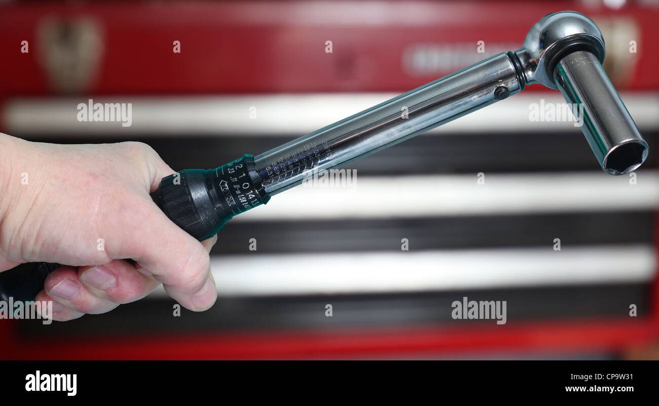 Mano d'uomo clenching chiave dinamometrica con cassettiera per utensili in background Foto Stock
