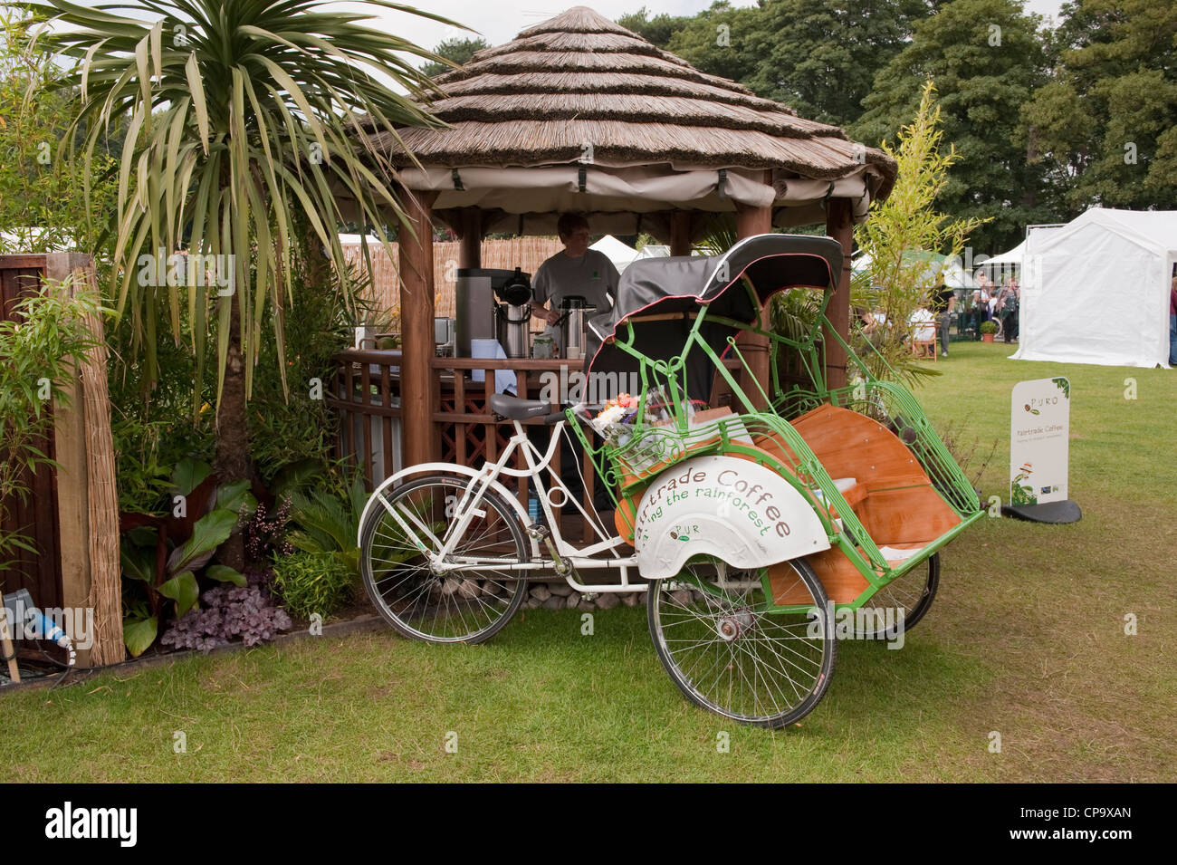 L'uomo lavora sul punto di ristoro (capanna con il tetto di paglia) vendita del caffè (trike per la telefonia mobile di servizio catering) - RHS Flower Show, Tatton Park, Cheshire, Inghilterra. Foto Stock