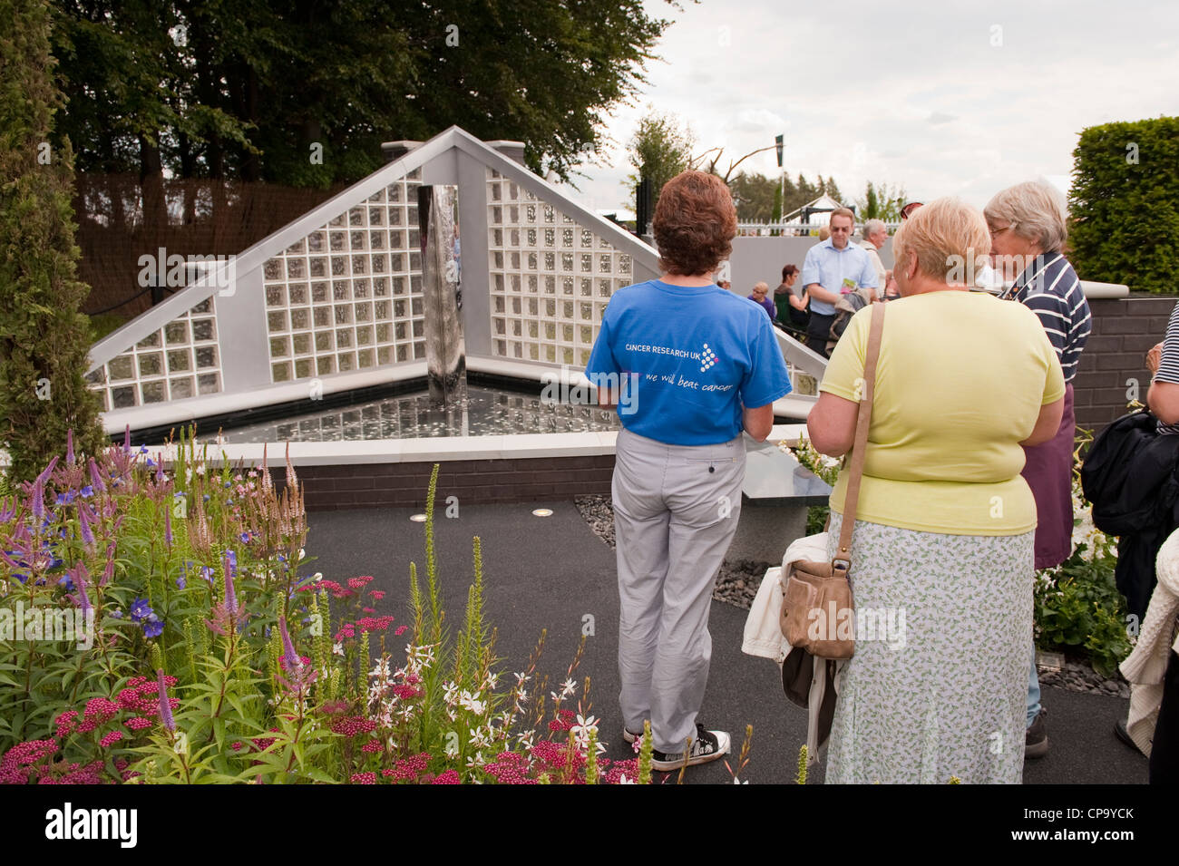 Persone in piedi con il lavoratore di volontariato, visualizzazione funzione acqua brillare in giardino per il Cancer Research UK - RHS Flower Show, Tatton Park, Cheshire, Inghilterra. Foto Stock