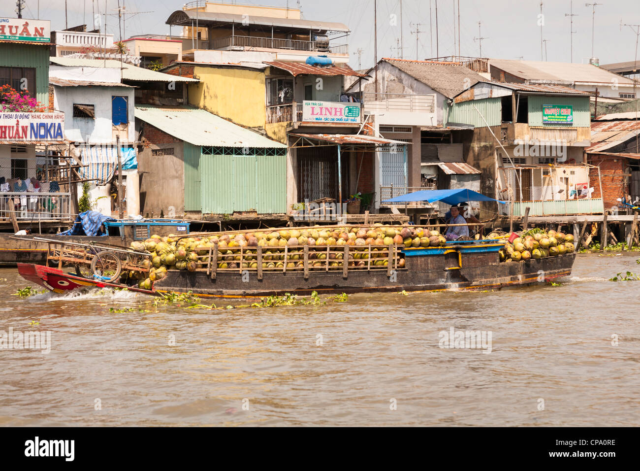 Barca laden con noci di cocco passando dai negozi e case, Cai Be, il fiume Mekong Delta, Vietnam Foto Stock