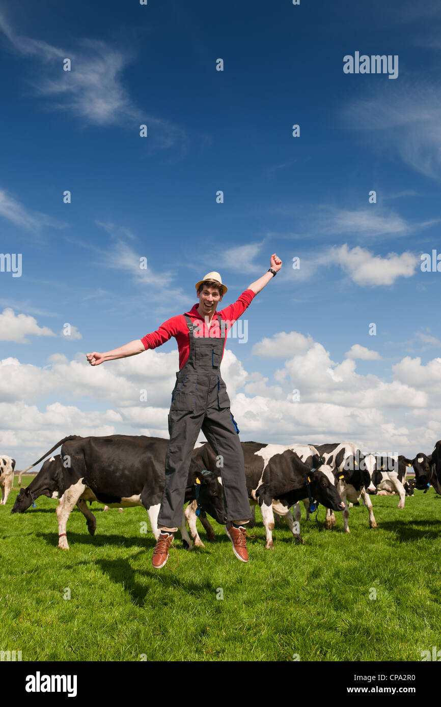 Felice giovane agricoltore il salto nel campo con le vacche Foto Stock