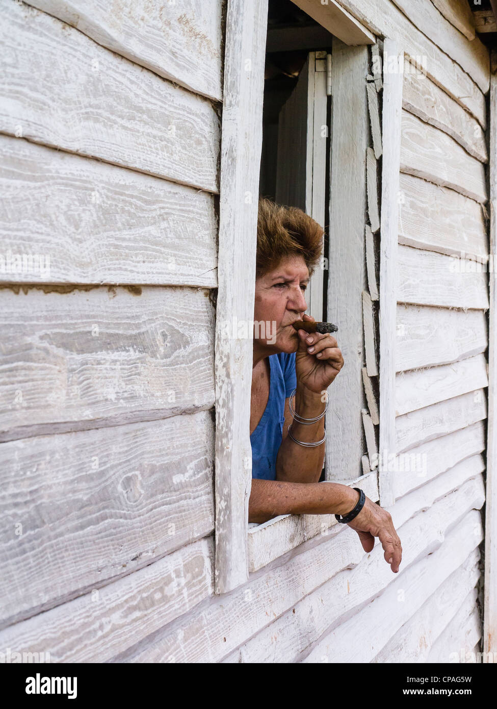 Un cubano femmina senior citizen si inclina fuori da una finestra aperta della sua facciata in legno casa di fumare un sigaro in Viñales, Cuba. Foto Stock
