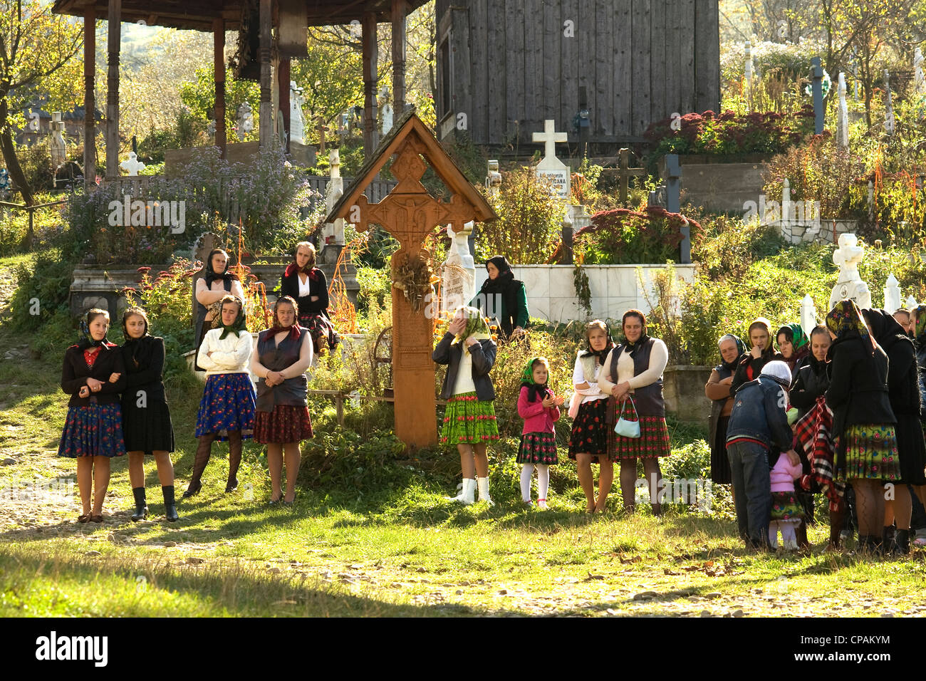 Donne e bambini rumeni, indossando i migliori abiti domenicali tradizionali nel cimitero ascoltando il servizio della chiesa a Botiza Foto Stock