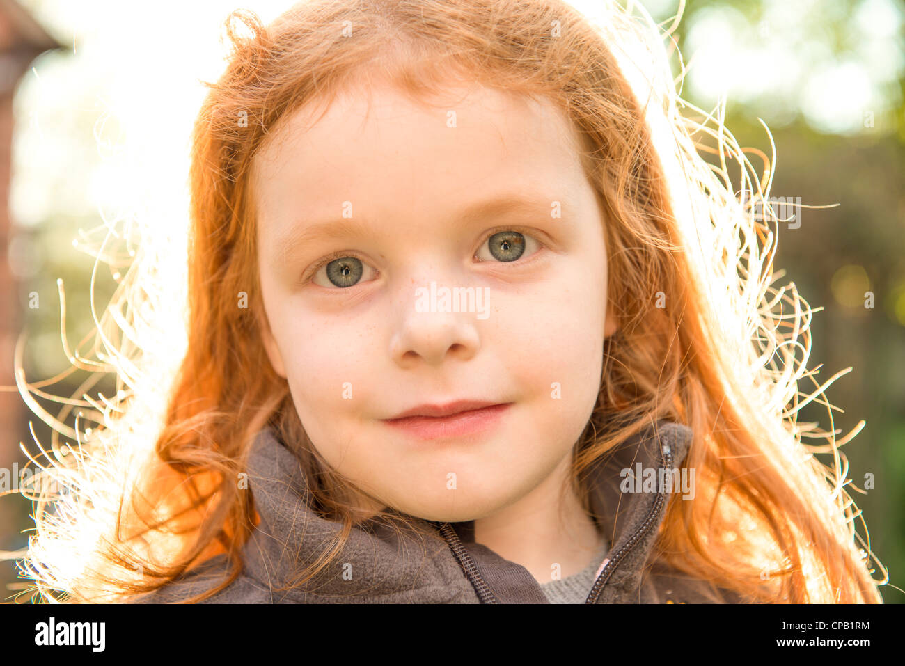 Bambina con zenzero capelli cercando di telecamera nel suo giardino estivo Foto Stock