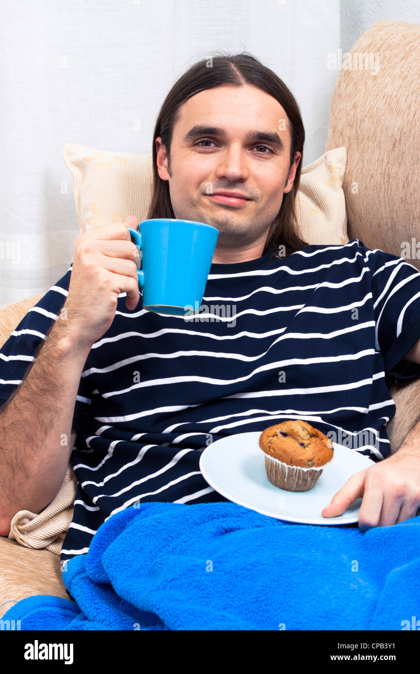 Giovane uomo avente la colazione ed il relax sul divano. Foto Stock