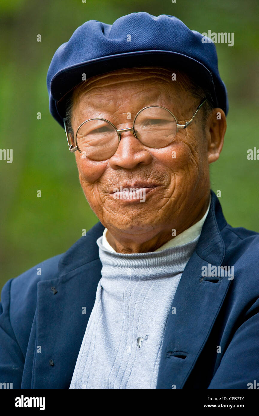 Un anziano uomo cinese vestito in abiti tradizionali con round occhiali rappresentano per la fotocamera in Pingliang. Foto Stock