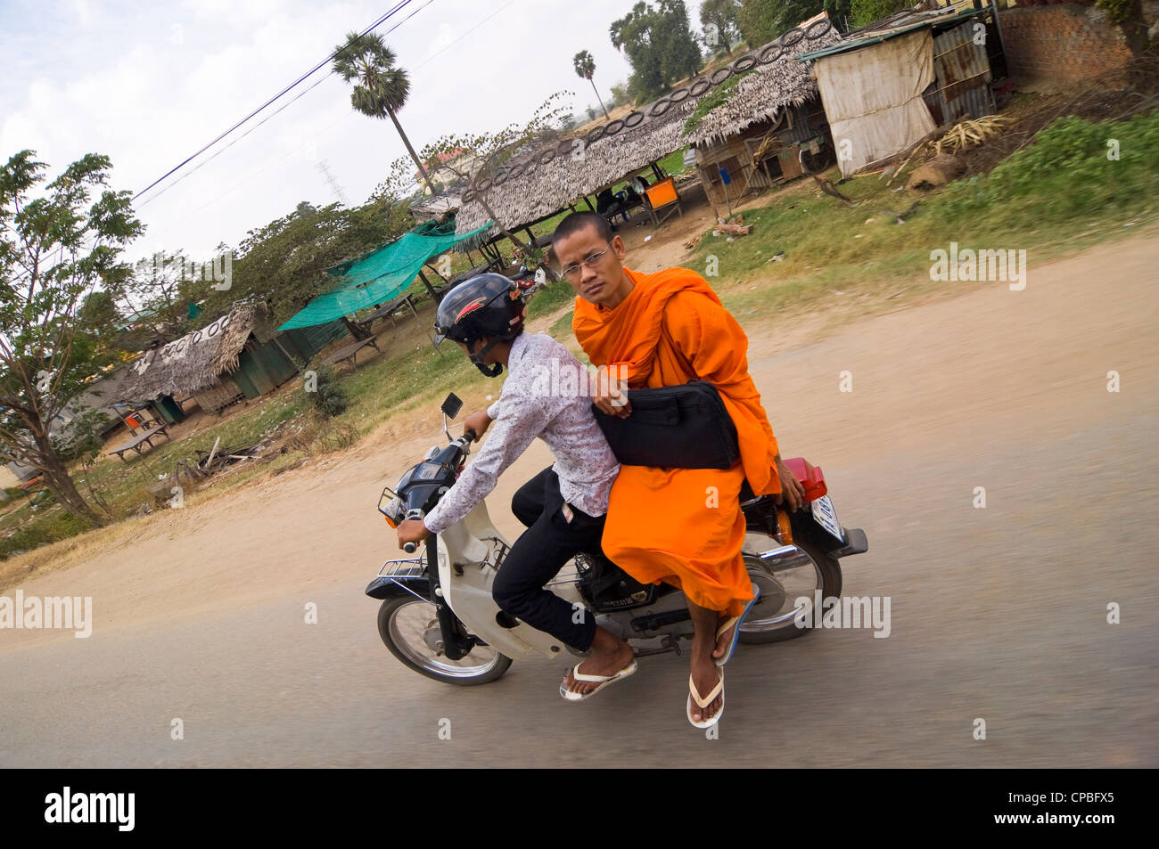 Ritratto orizzontale di un monaco buddista in sella come un pillion passeggero a bordo di un ciclomotore guidando lungo una strada in Cambogia. Foto Stock