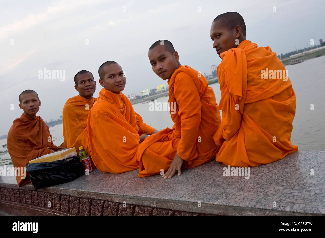 Ritratto orizzontale di cinque cambogiano di monaci buddisti seduta sulle sponde del fiume Tonle Sap per guardare il sole che tramonta. Foto Stock