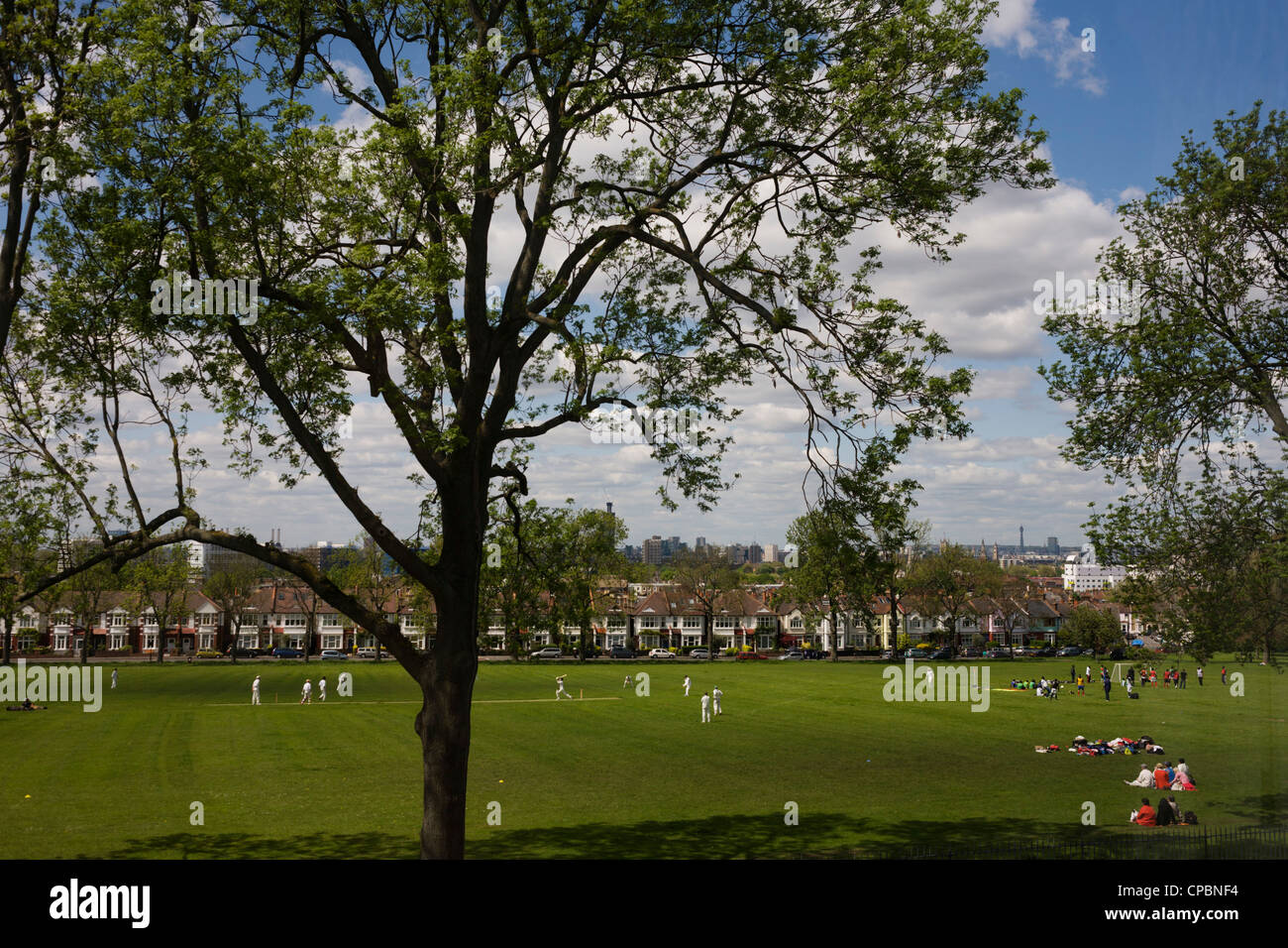 Una partita locale di cricket è giocato sull'erba verde sotto 100 anno-vecchio coppia frassini in Ruskin Park. Foto Stock