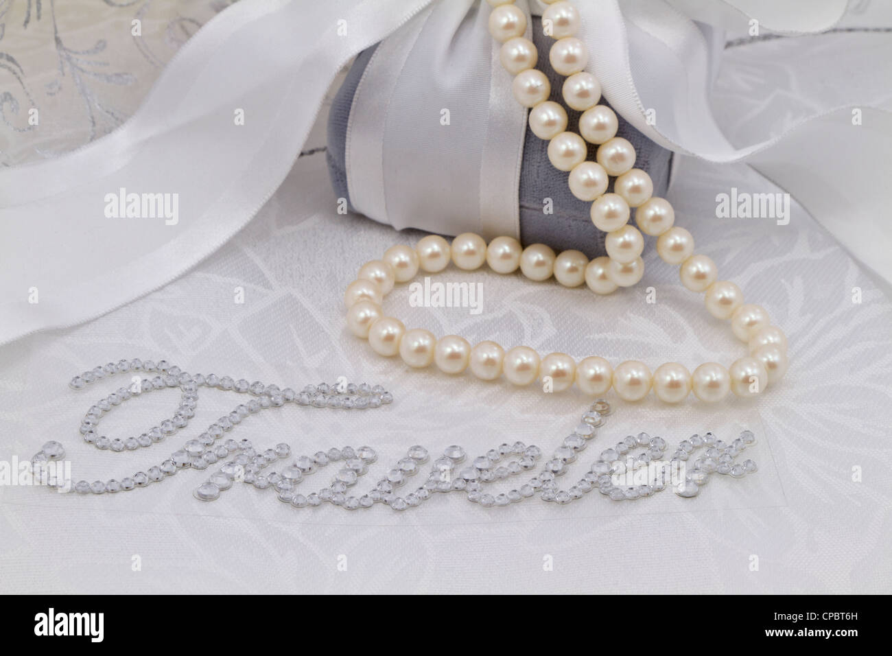 Immagine femminile con la parola "Traveler" in finti diamanti immessi sul damasco bianco e circondato da perle, velluto confezione regalo. Foto Stock