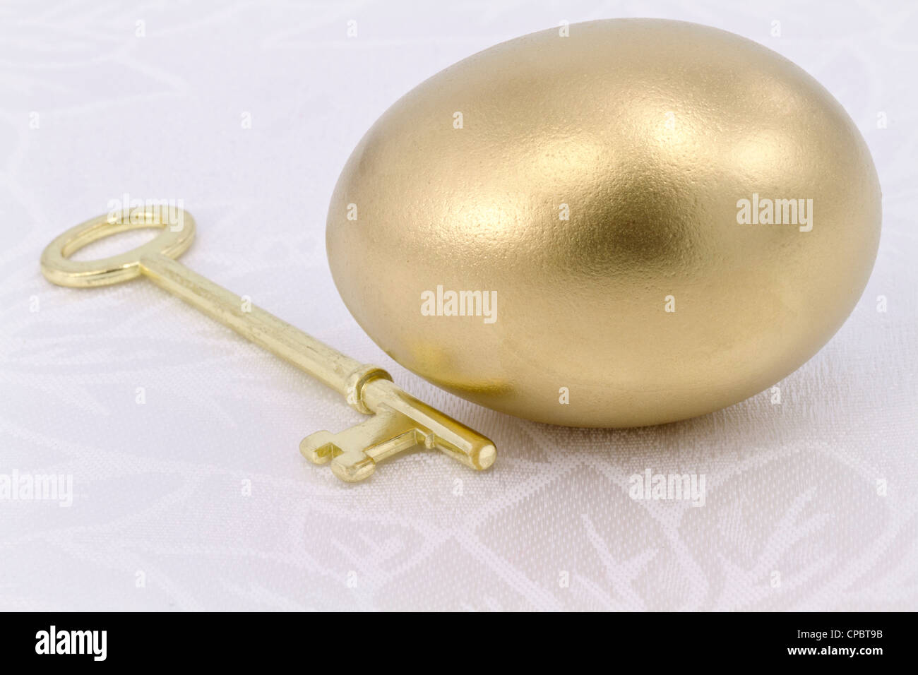 Close up luccicanti uovo d'oro lucido con chiave sul panno bianco; metafora di soluzione e di successo, di speranza e di opportunità. Foto Stock