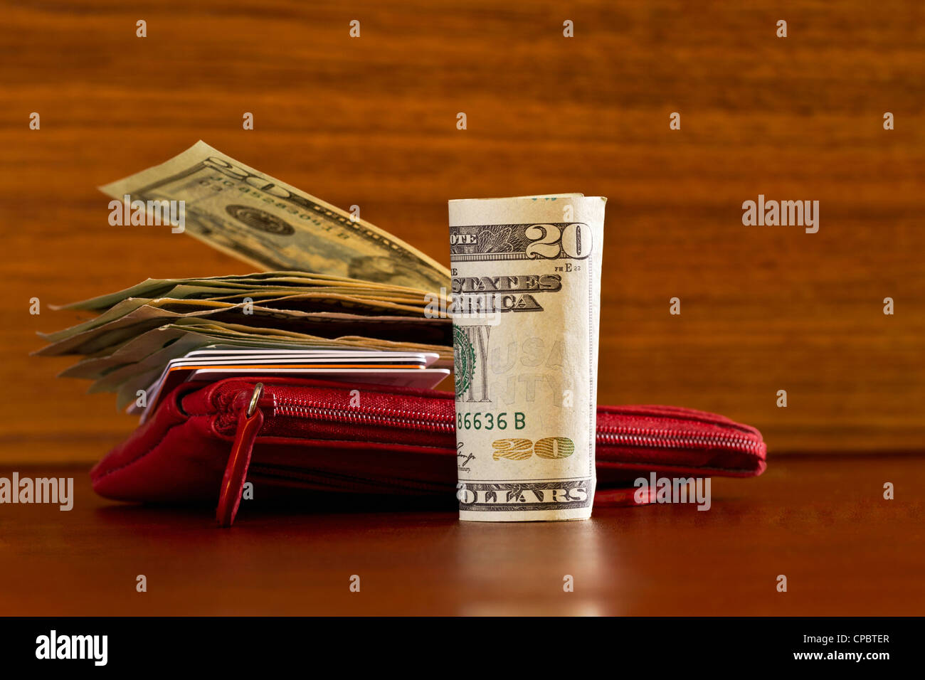 Moneta americana con carte di credito poste su e attorno al rosso wallet su legno grano; immagine del consumatore moderno o elementi shopper. Foto Stock