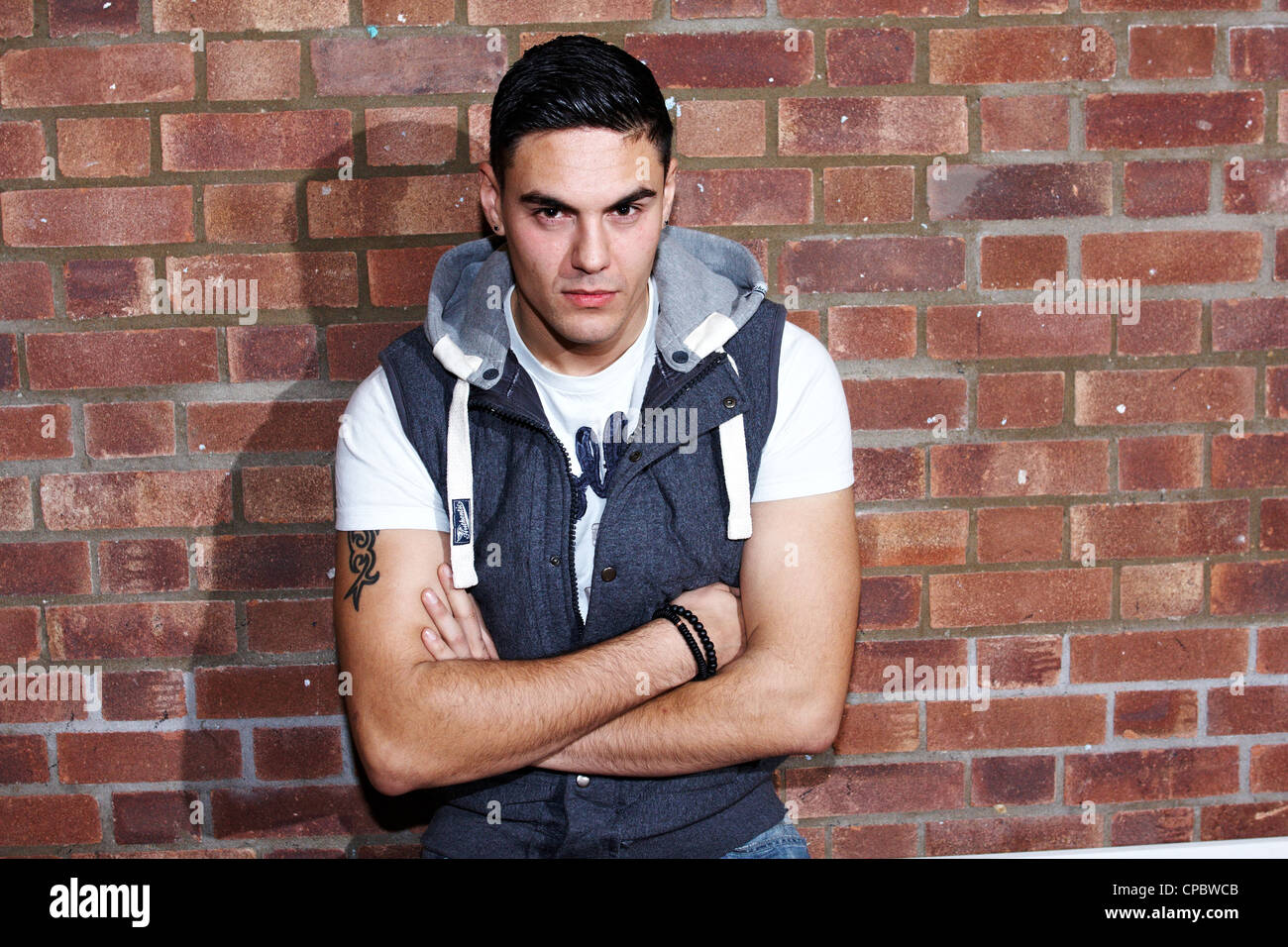 Ritratto di un uomo bianco in un top con cappuccio contro un muro di mattoni di sfondo (non ritoccate). Foto Stock