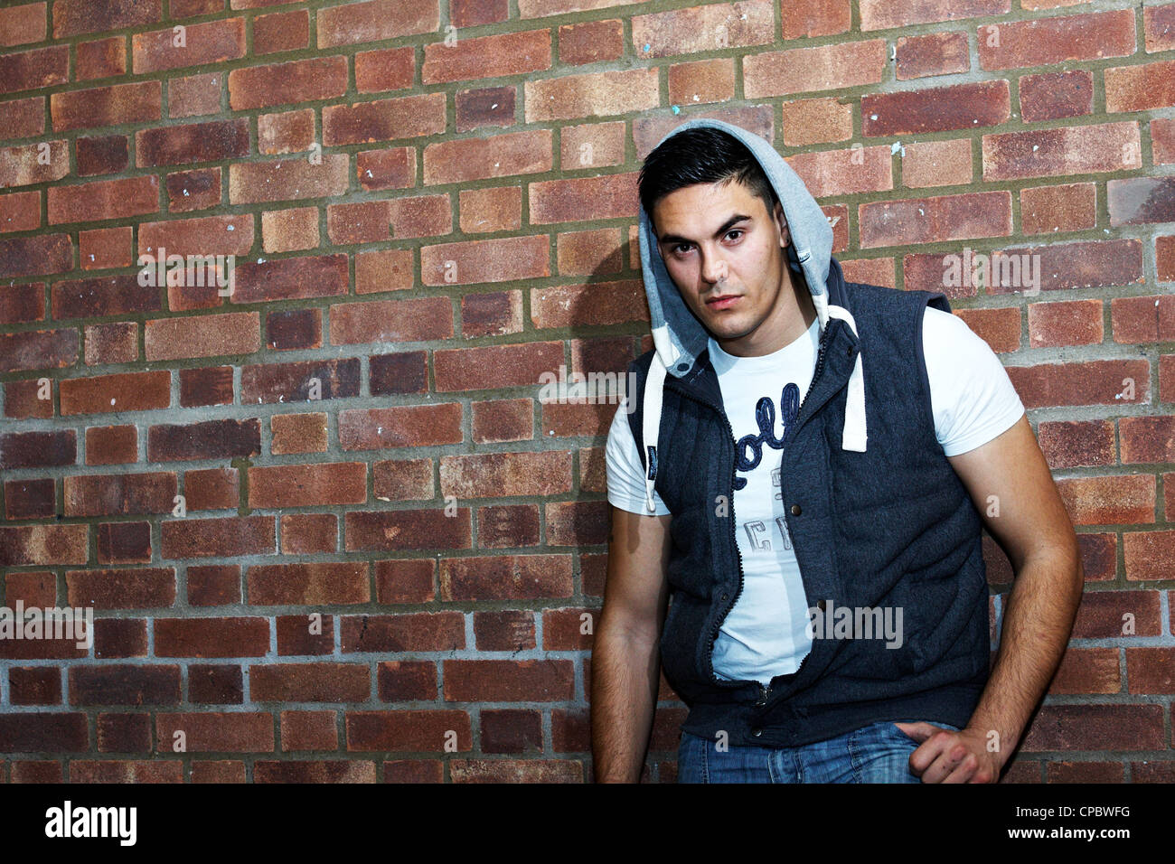 Ritratto di un uomo bianco in un top con cappuccio contro un muro di mattoni di sfondo (non ritoccate). Foto Stock