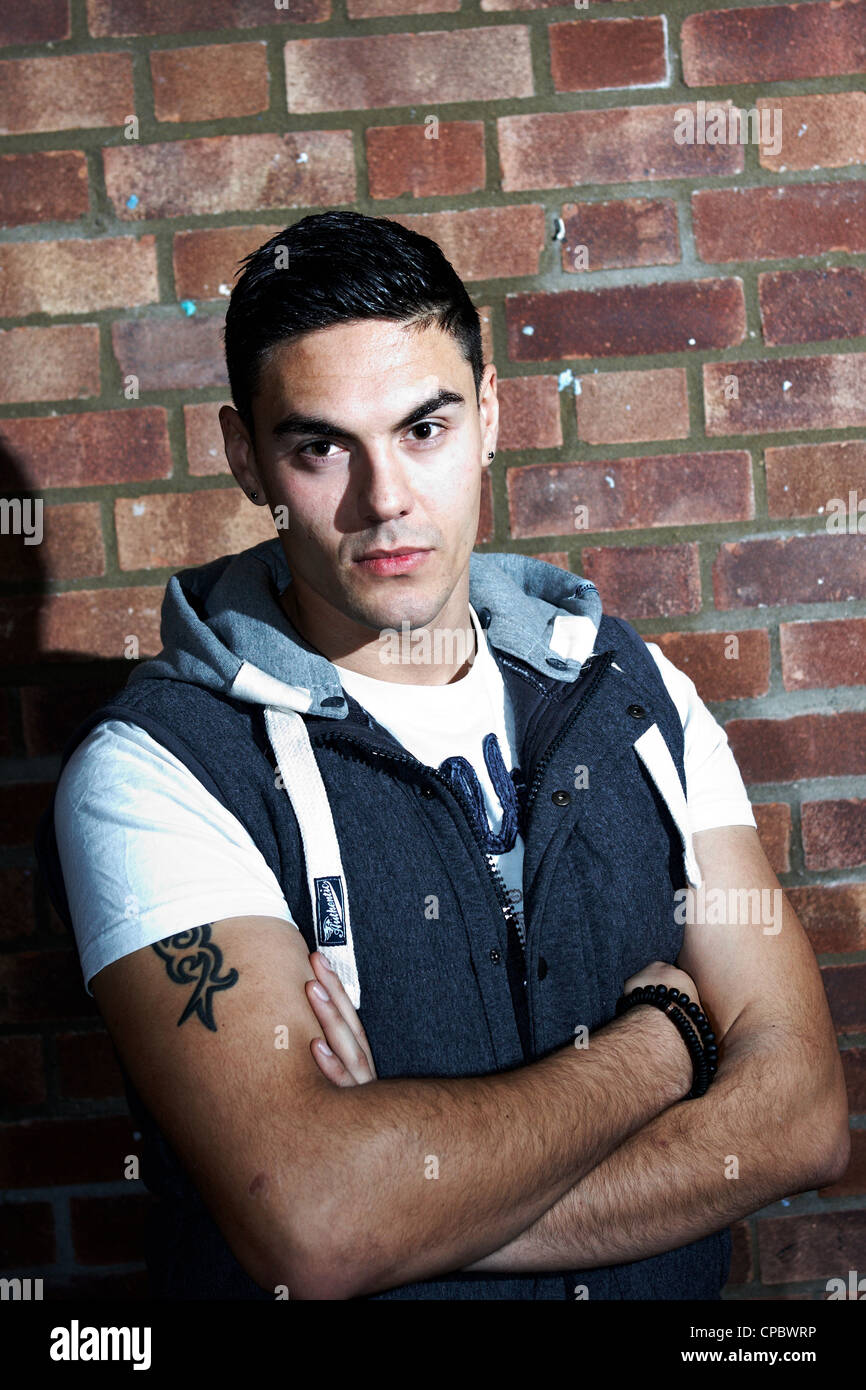 Ritratto di un uomo bianco in un top con cappuccio contro un muro di mattoni di sfondo (non ritoccate). Foto Stock