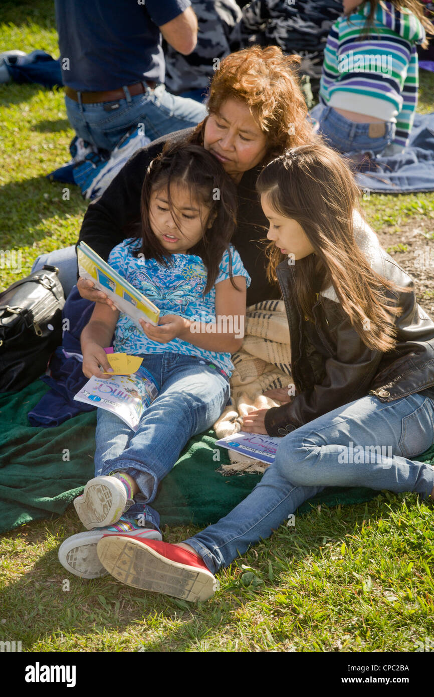 La mamma si unisce le sue due figlie ispanica con lettura a una piscina esterna 'Dr. Seuss annuale Fiera di alfabetizzazione' in una scuola di Westminster, ca. Foto Stock