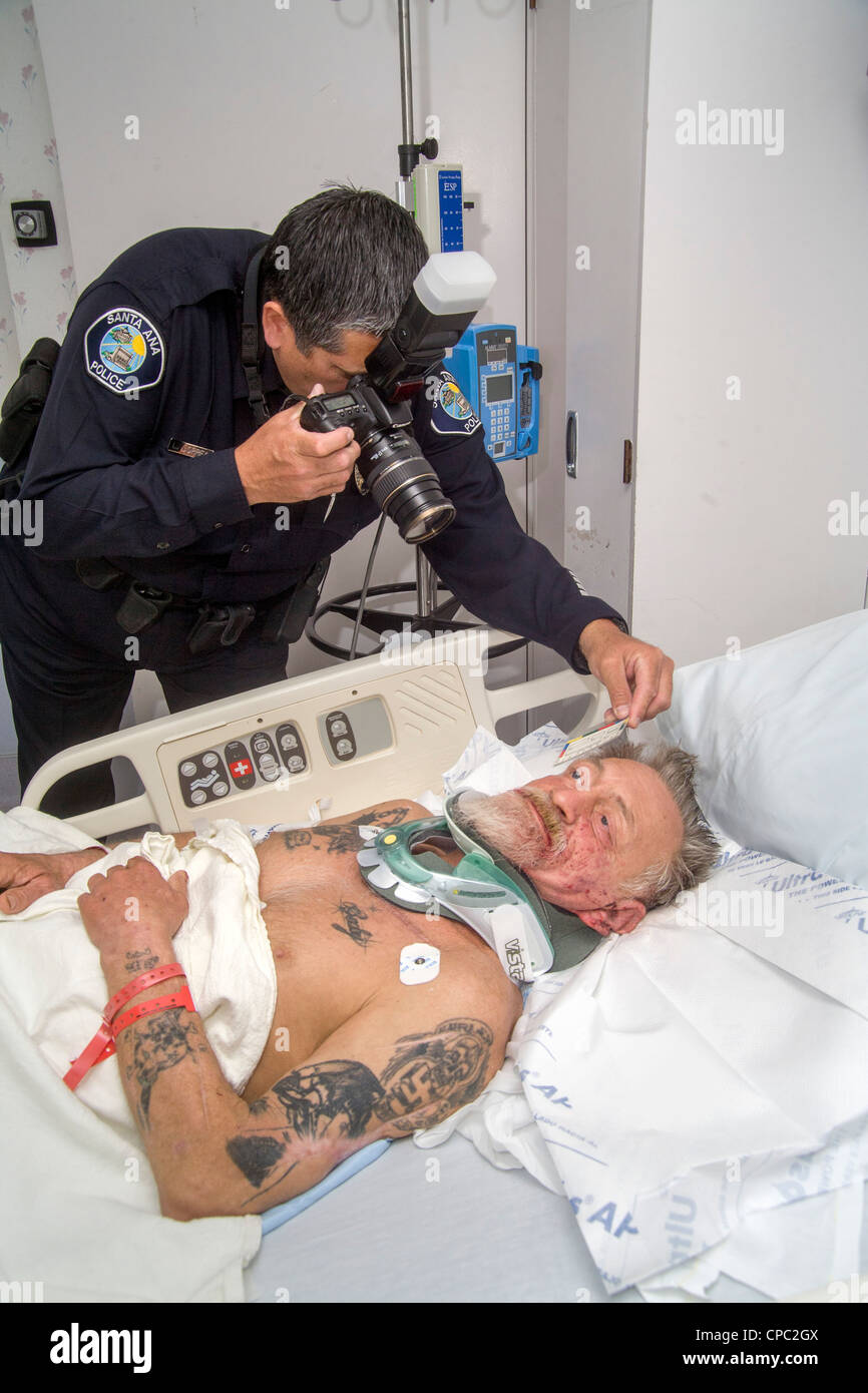 In un ospedale locale di una polizia ispanica investigatore della scena del crimine fotografie delle lesioni di un anziano uomo senza tetto assault vittima. Foto Stock