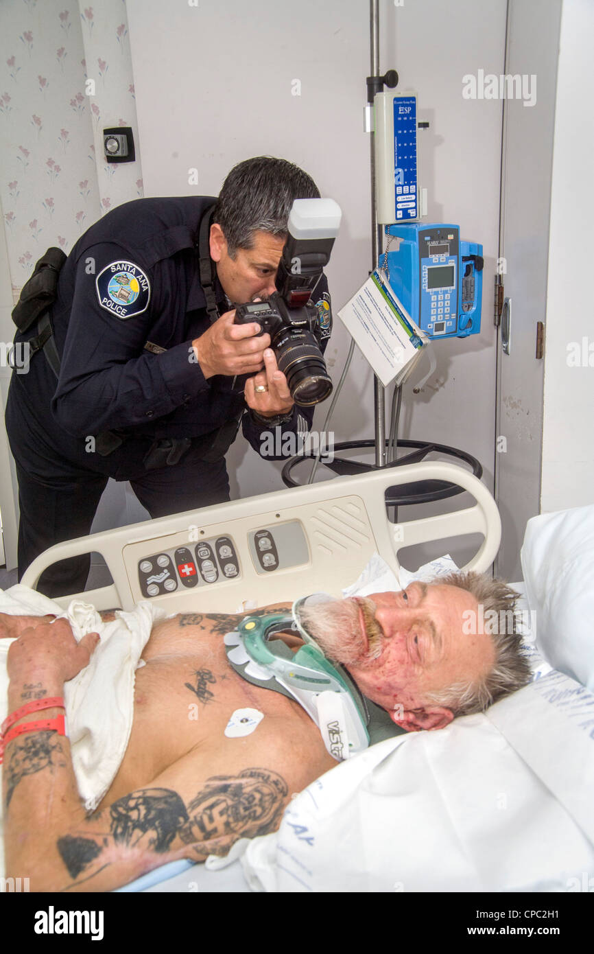 In un ospedale locale di una polizia ispanica investigatore della scena del crimine fotografie delle lesioni di un anziano uomo senza tetto assault vittima. Foto Stock