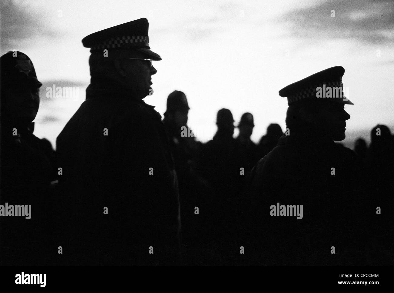Silhouette di due alti funzionari di polizia che compongono la presenza delle forze di polizia come alba sorge a Stonehenge Solstice, Wilts, nel 1985. Foto Stock