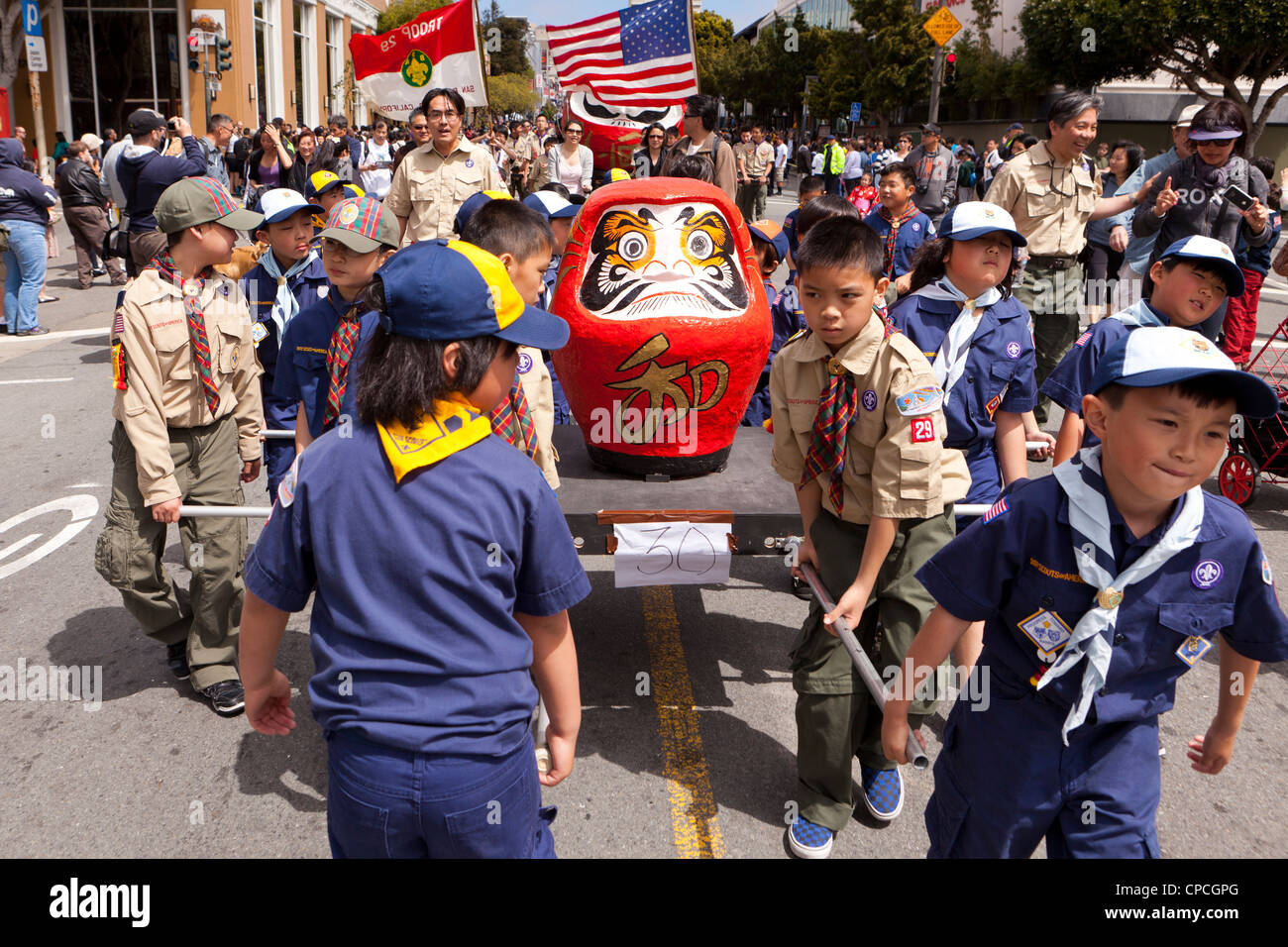 Japanese-American boy scout portando una grande bambola Daruma figura durante un festival culturale parade Foto Stock