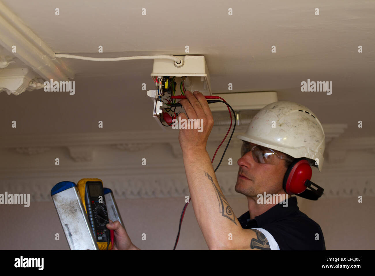 Un elettricista in sostituzione di una luce di emergenza su di un soffitto in area comunale Foto Stock