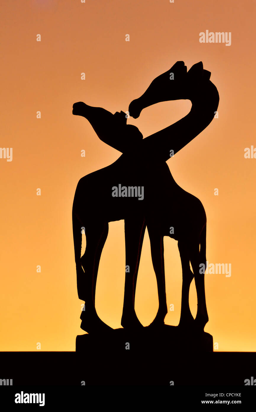 Scultura in legno di due paesi africani le giraffe stagliano contro il cielo arancione al tramonto Foto Stock