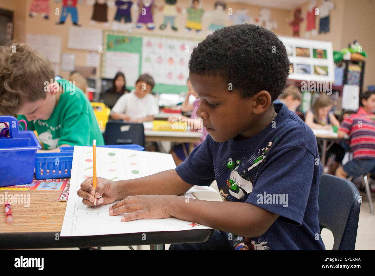 Maschio afro-americano kindergarten studente lavora al suo banco durante le lezioni al Texas pubblico scuola elementare Foto Stock