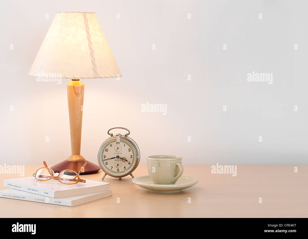 Lampada da tavolo, tazzina, orologio, occhiali e libri sul tavolo Foto Stock