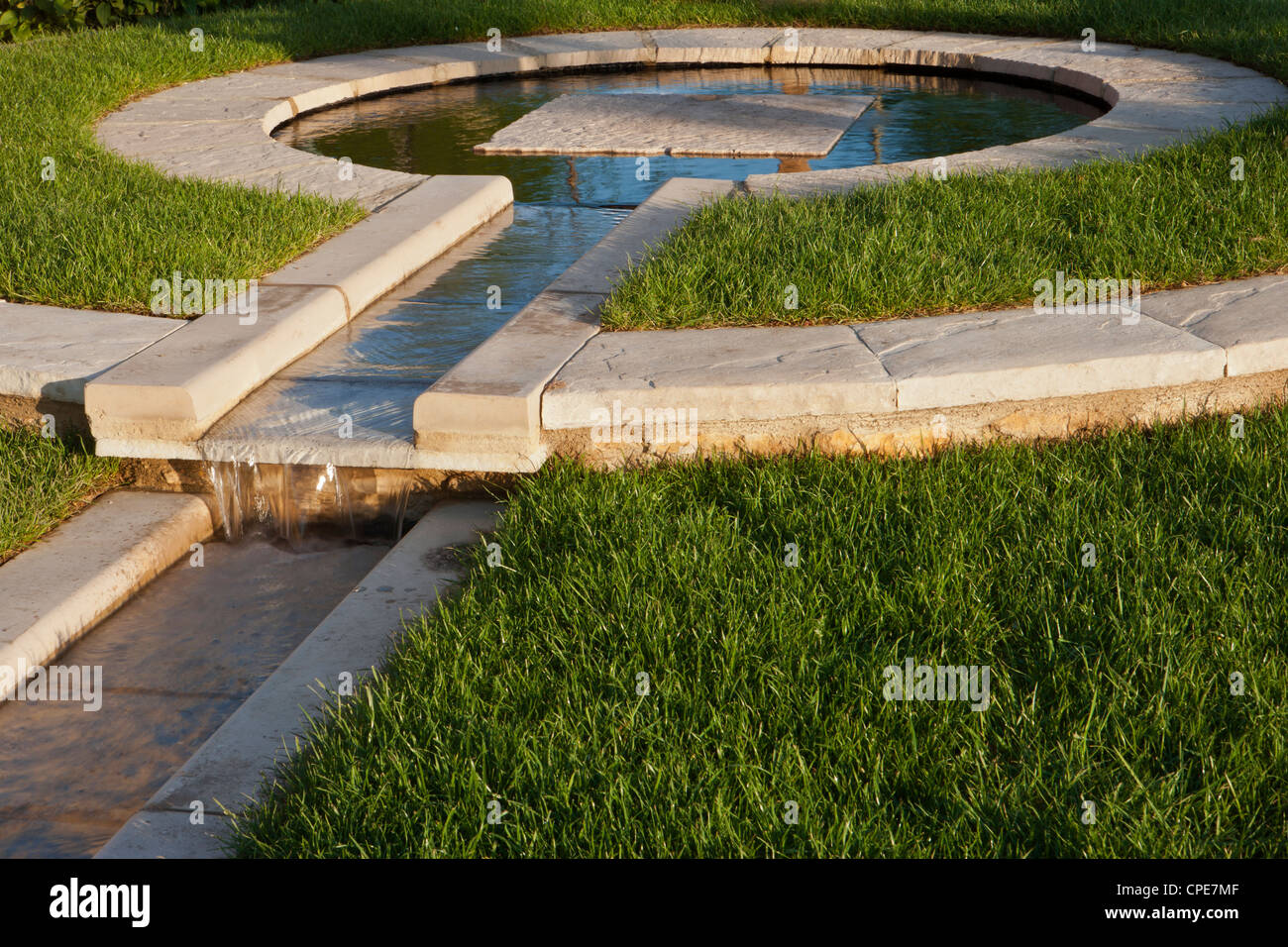 Un giardino con laghetto circolare, un giardino con fontana in pietra e pavimentazione pavimentata che delimitano prati del Regno Unito Foto Stock