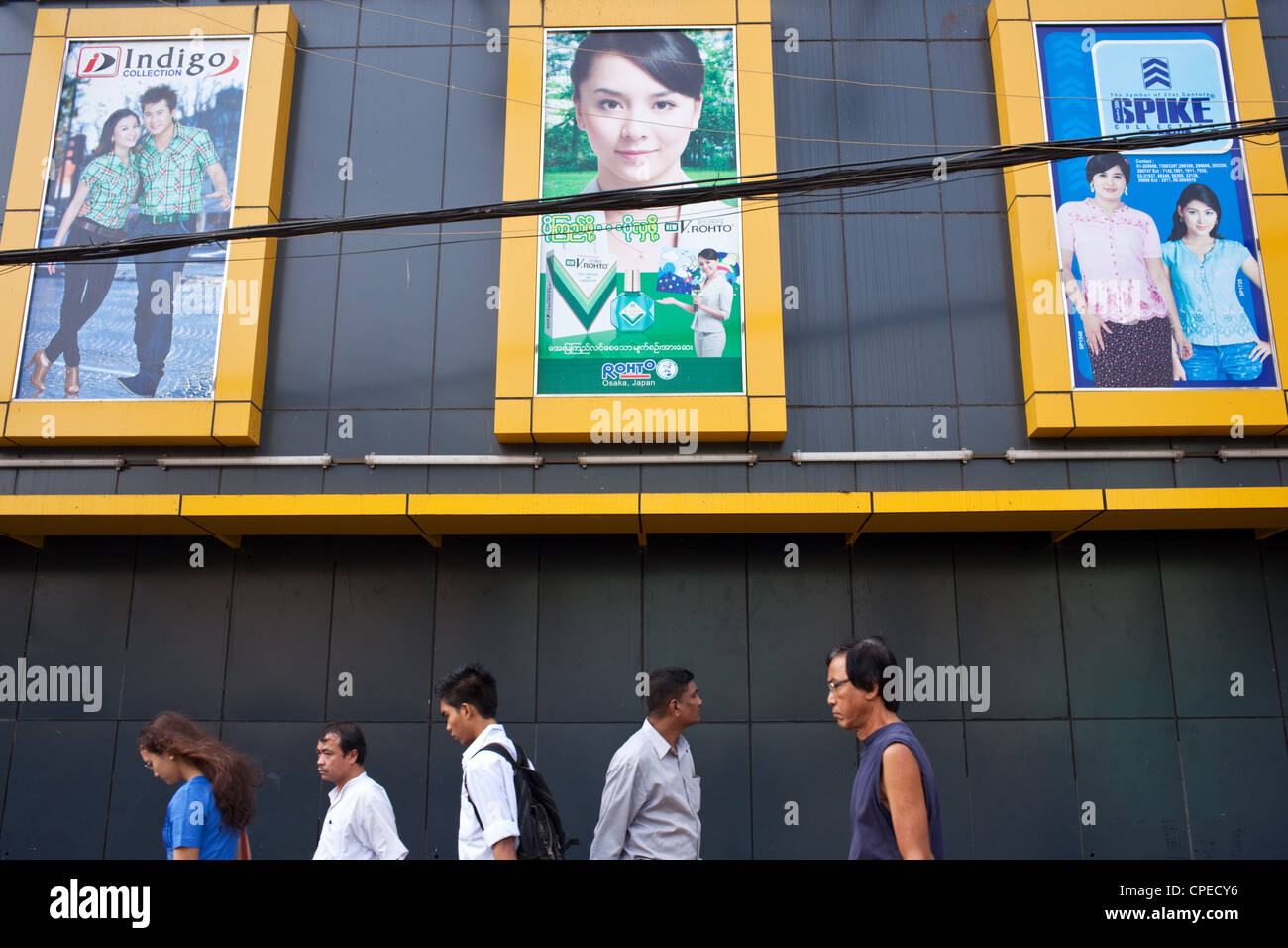 Popolo birmano a piedi sotto i manifesti pubblicità abbigliamento nel centro di Yangon (Rangoon), Myanmar (Birmania) Foto Stock