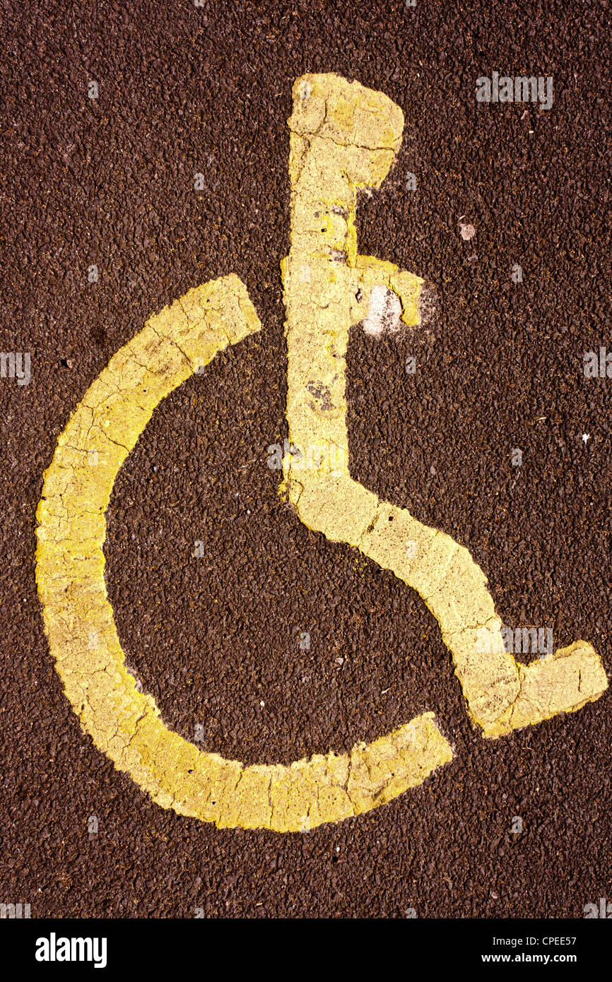 Un parcheggio disabili bay con l'icona di una sedia a rotelle, dipinto di giallo su rosso tarmacadam. Foto Stock