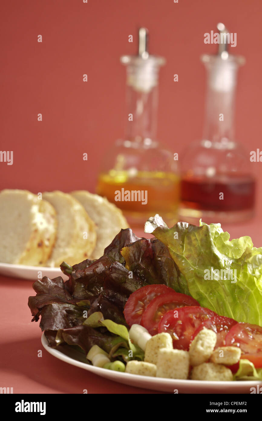 Una insalata di lattuga con fette di pane di pasta acida e una ampolla di olio e aceto su un soffice rose sfondo colorato. Foto Stock