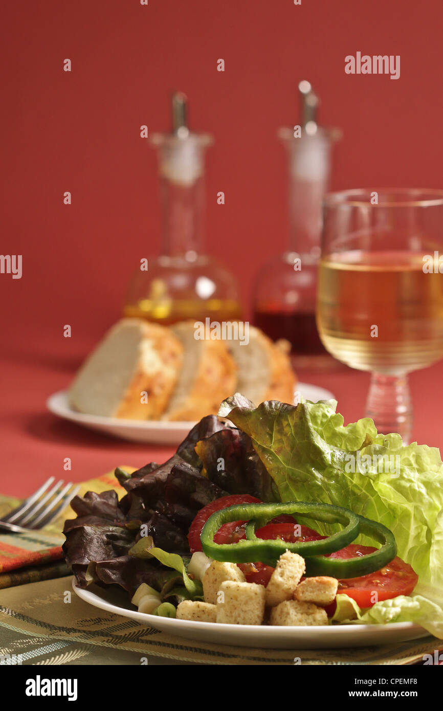 Un luogo impostazione di insalata, pane e vino su di una rosa colore di sfondo. Foto Stock