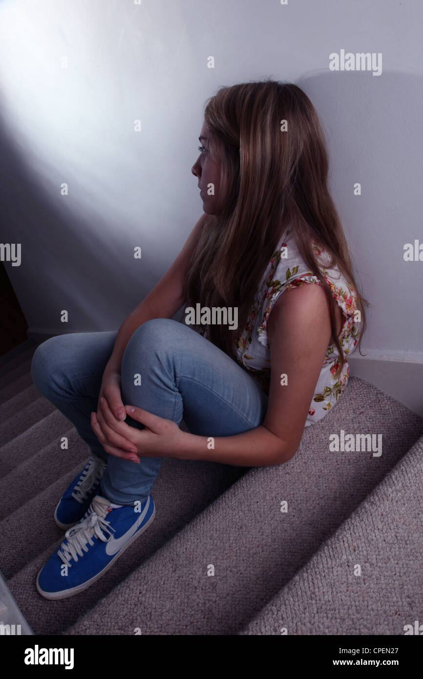 Giovane ragazza seduta sulle scale scuro vista posteriore Foto Stock