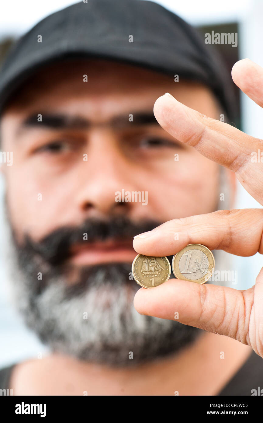 Cafe Proprietario Nikos Bourbakis tenendo una vecchia moneta dracma sostituito dall'euro nel 2002 e un greco euro moneta. Foto Stock