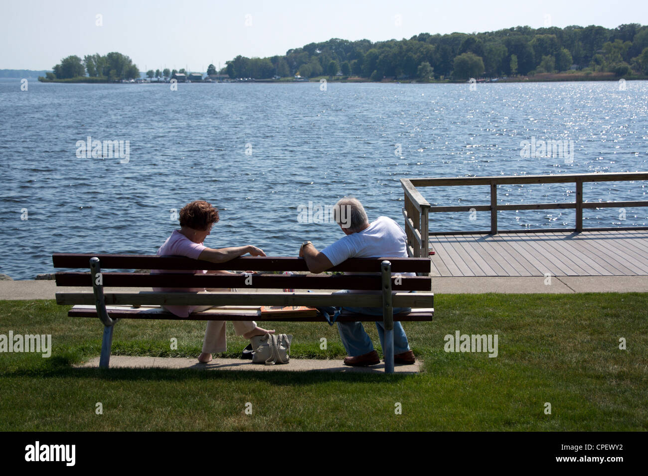 Coppia di anziani seduti su una panchina nel parco affacciato sul lago bianco vicino a Whitehall, MI Foto Stock