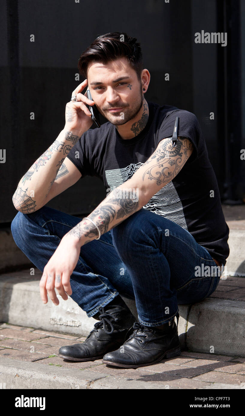 A piena lunghezza Ritratto di una giovane alla moda uomo seduto e a parlare su un telefono cellulare, Spitalfields, London, England, Regno Unito Foto Stock
