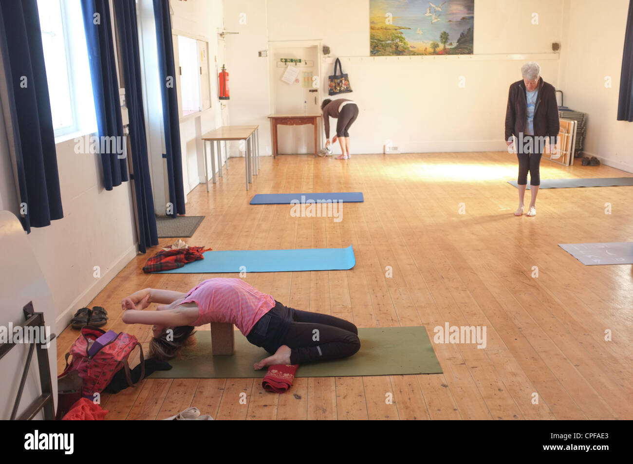 Una donna nella sua metà degli anni quaranta si riscalda prima di una lezione di yoga tenuto in un villaggio hall in Cornwall, Regno Unito Foto Stock