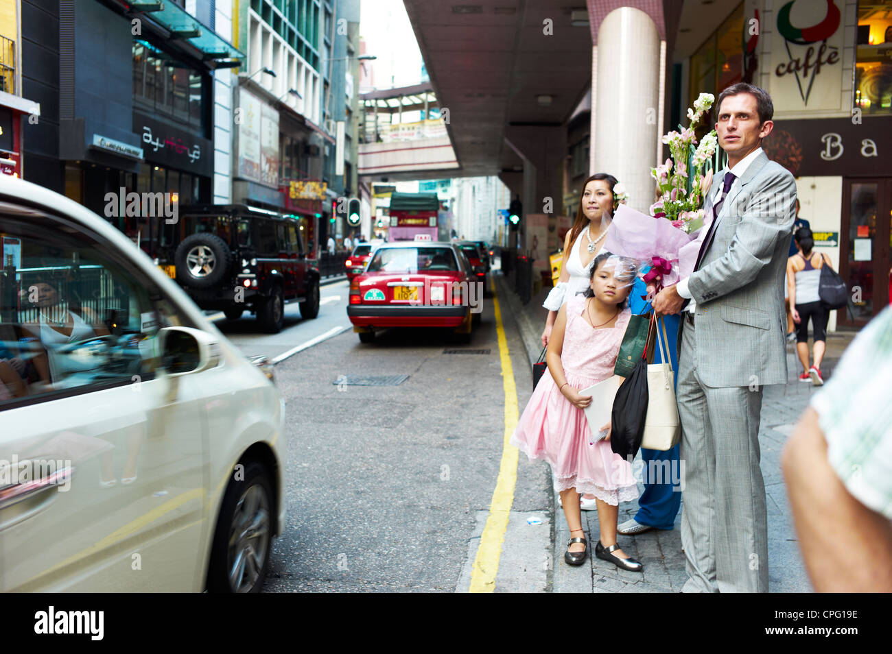 Una famiglia vestite per un evento formale attende un taxi in centro a Hong Kong. Foto Stock