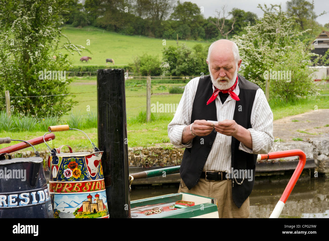 Canal Boat uomo la laminazione di una sigaretta indossando abiti periodo su una piccola imbarcazione durante il Rickmansworth annuale festival di canale Foto Stock