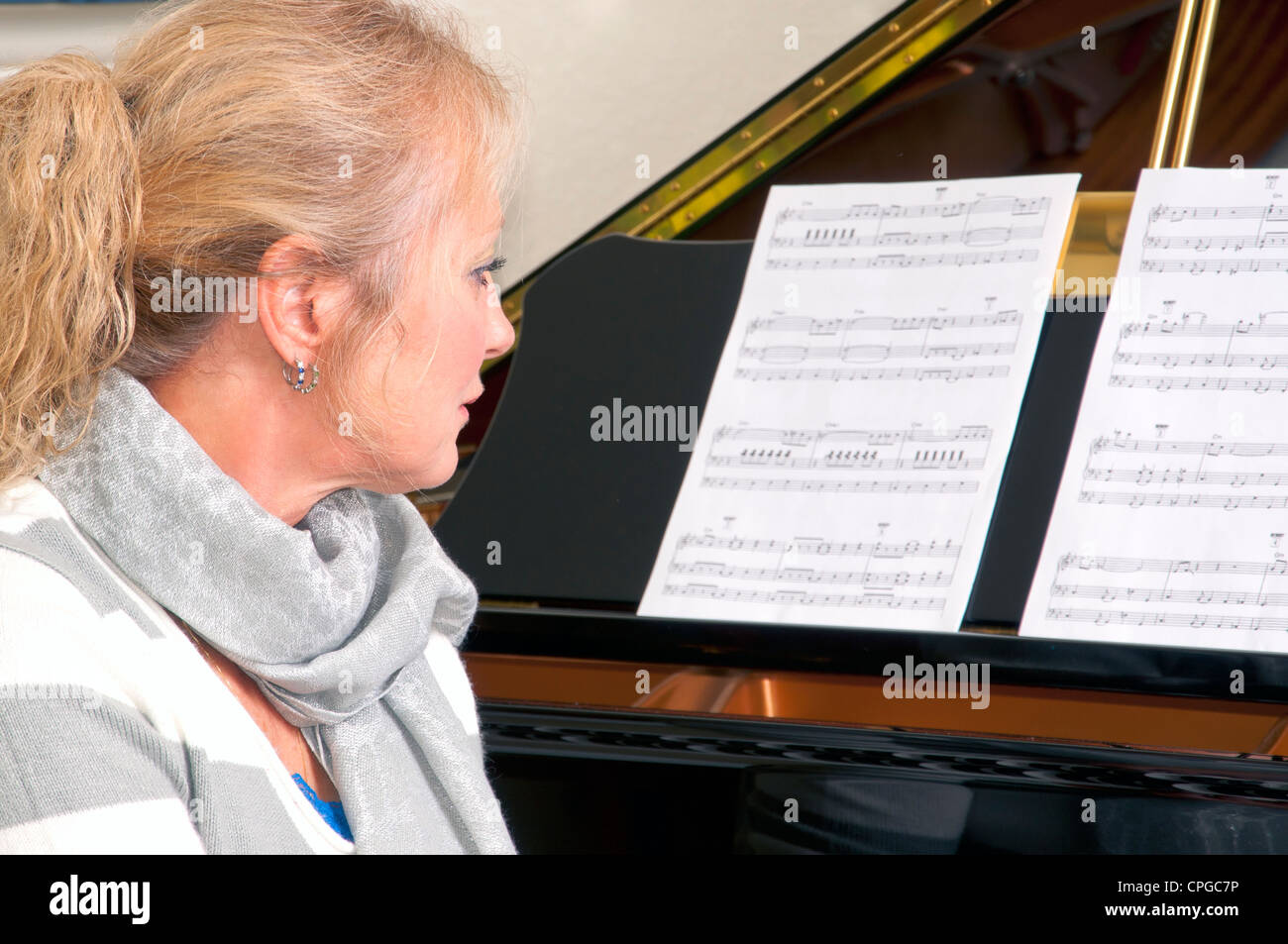 Attraente donna bionda seduto a un grande pianoforte guardando il foglio di musica. Foto Stock