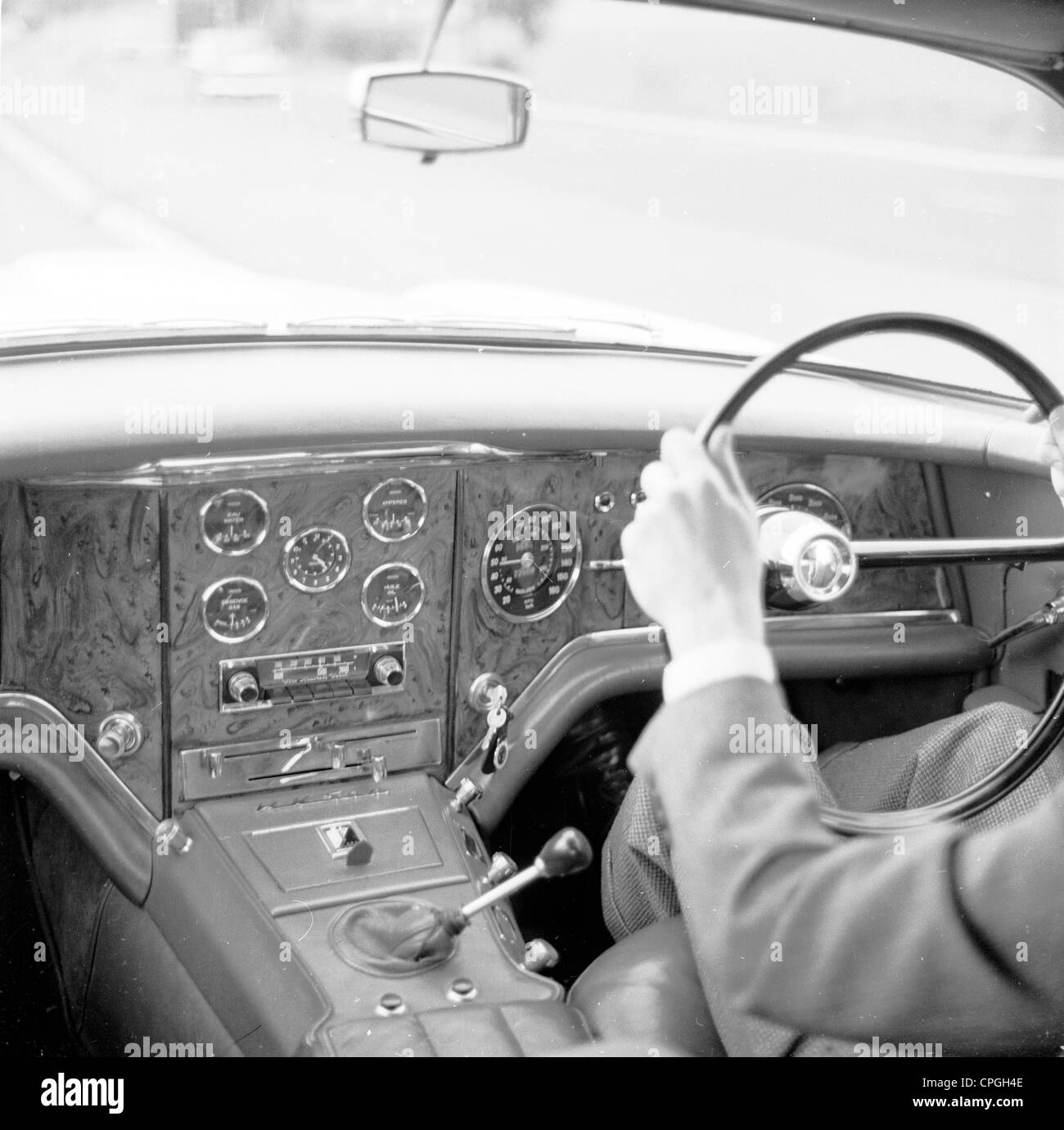 Anni sessanta, storico vista interna di interni in legno dash o sul cruscotto di un Facel-Vega auto sportiva, con driver maschio (fuori dall'inquadratura) al volante. Foto Stock