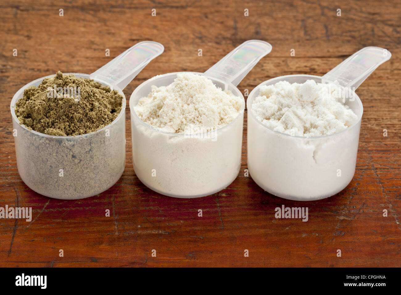 Misurazione di plastica scoop di tre proteine in polvere (da sinistra i semi di canapa, il siero di latte concentrato, il siero di latte isolare) su un grunge superficie di legno Foto Stock