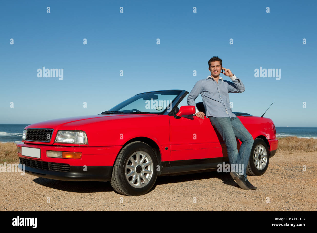 Uomo che utilizza il telefono cellulare, appoggiata contro un rosso convertibili. Foto Stock