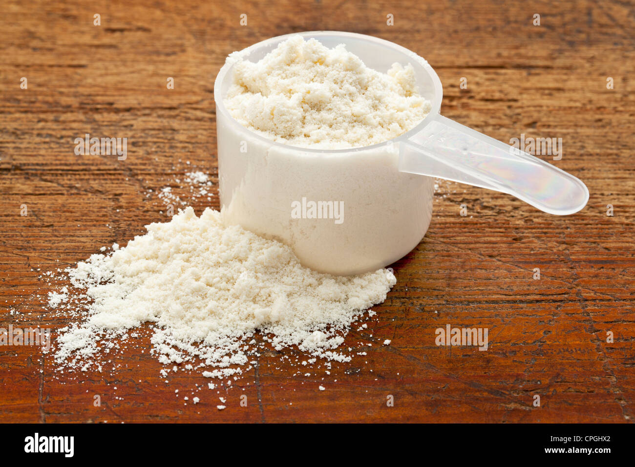 Plastica misurino di polvere bianca (proteina di siero di latte) contro il grunge Sfondo legno Foto Stock