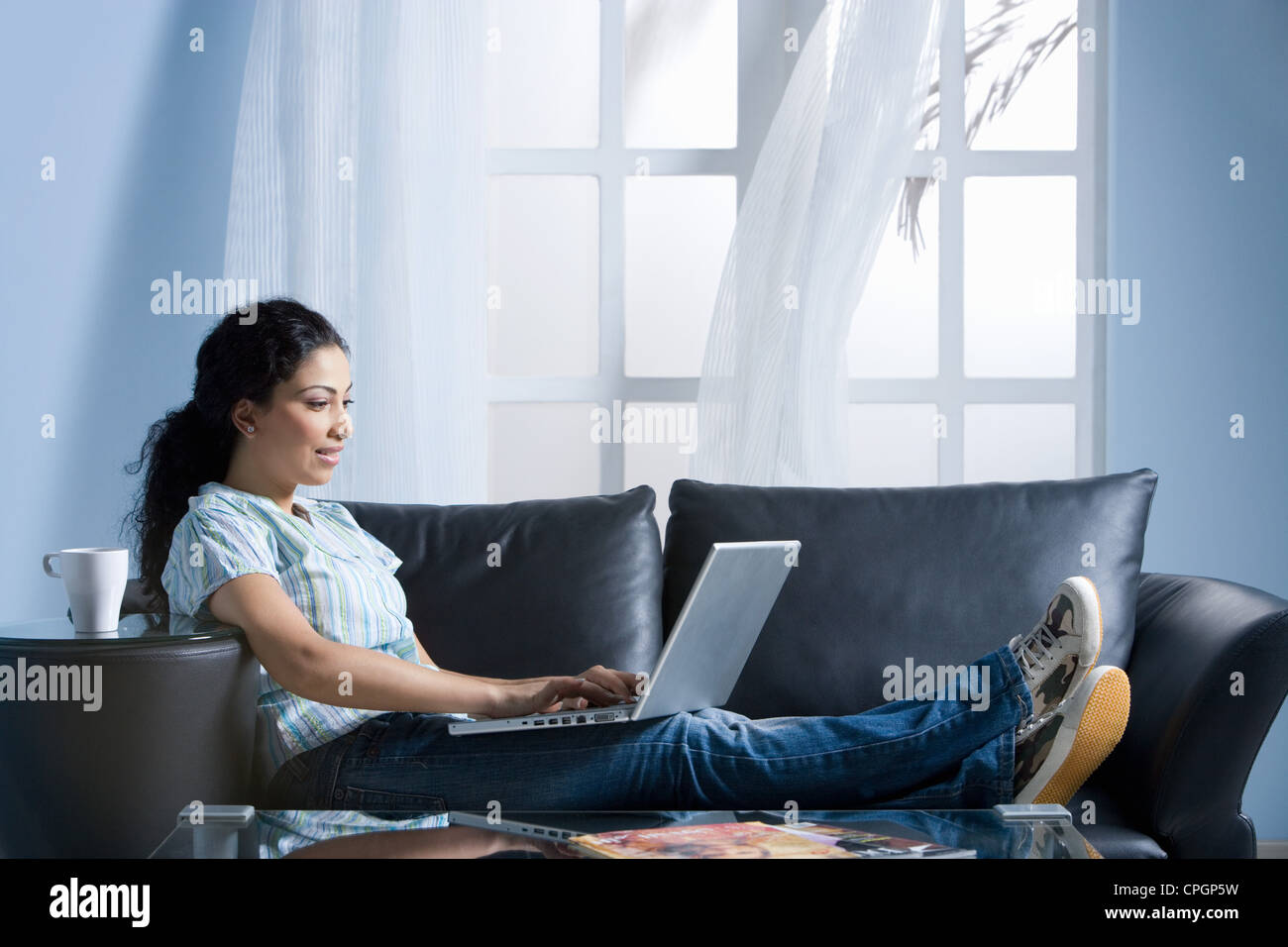 Giovane donna utilizzando computer portatile sul divano Foto Stock