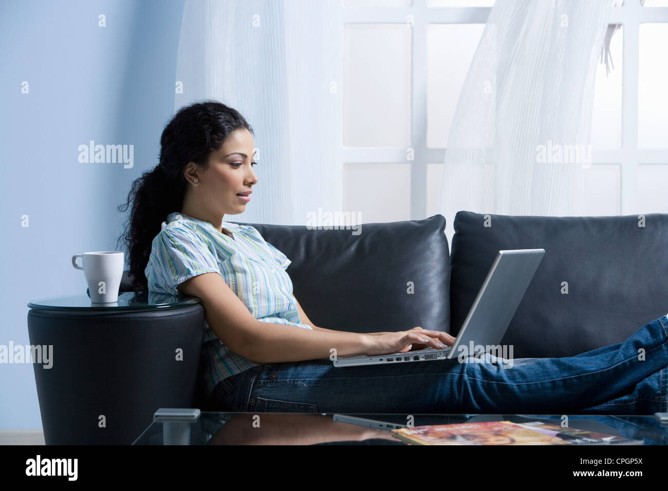 Giovane donna utilizzando computer portatile sul divano Foto Stock